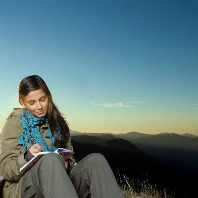 Studentin schreibt auf einem Berggipfel in ihrem Tagebuch
