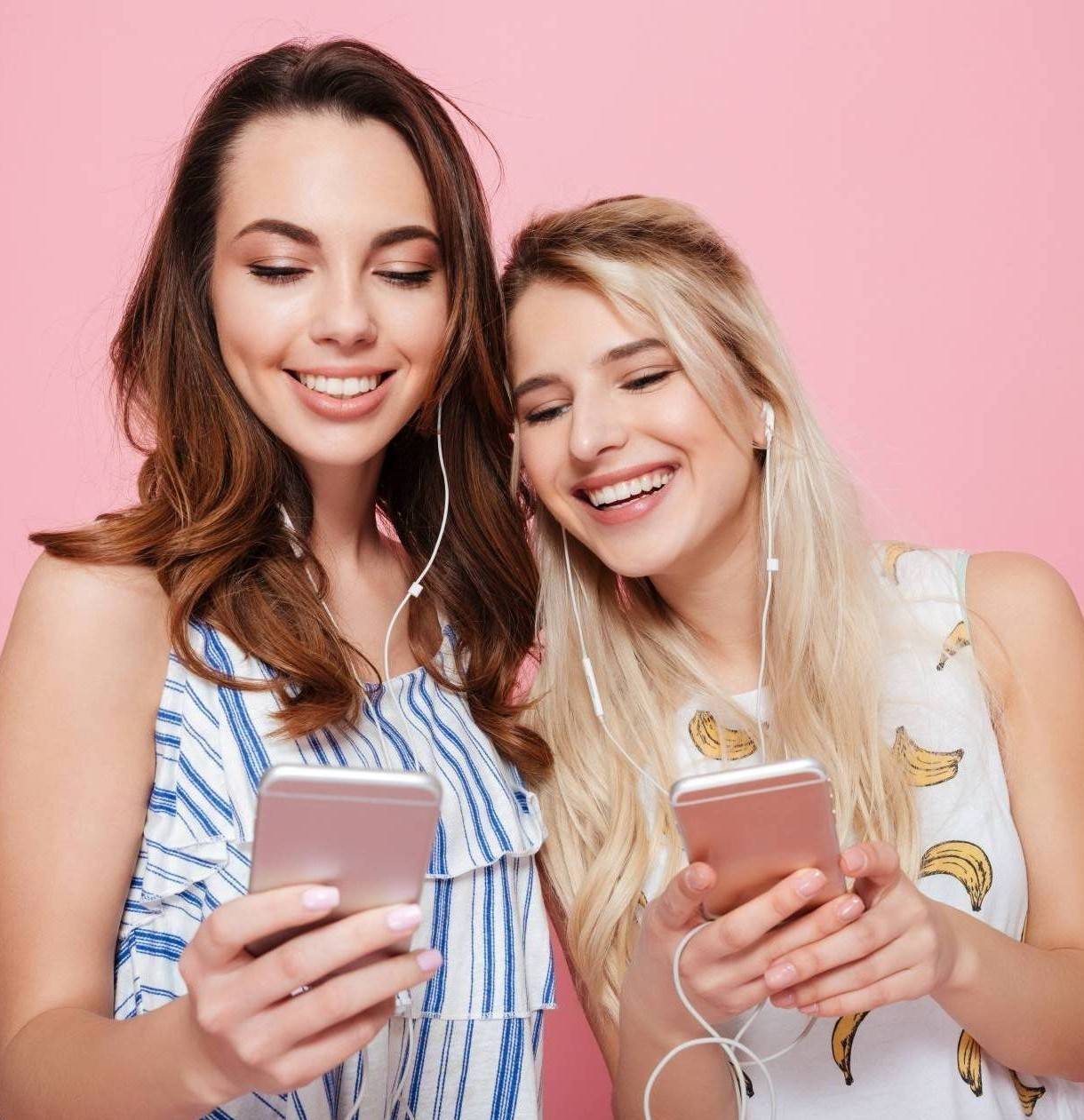 Zwei junge Frauen hören einen Podcast und lächeln