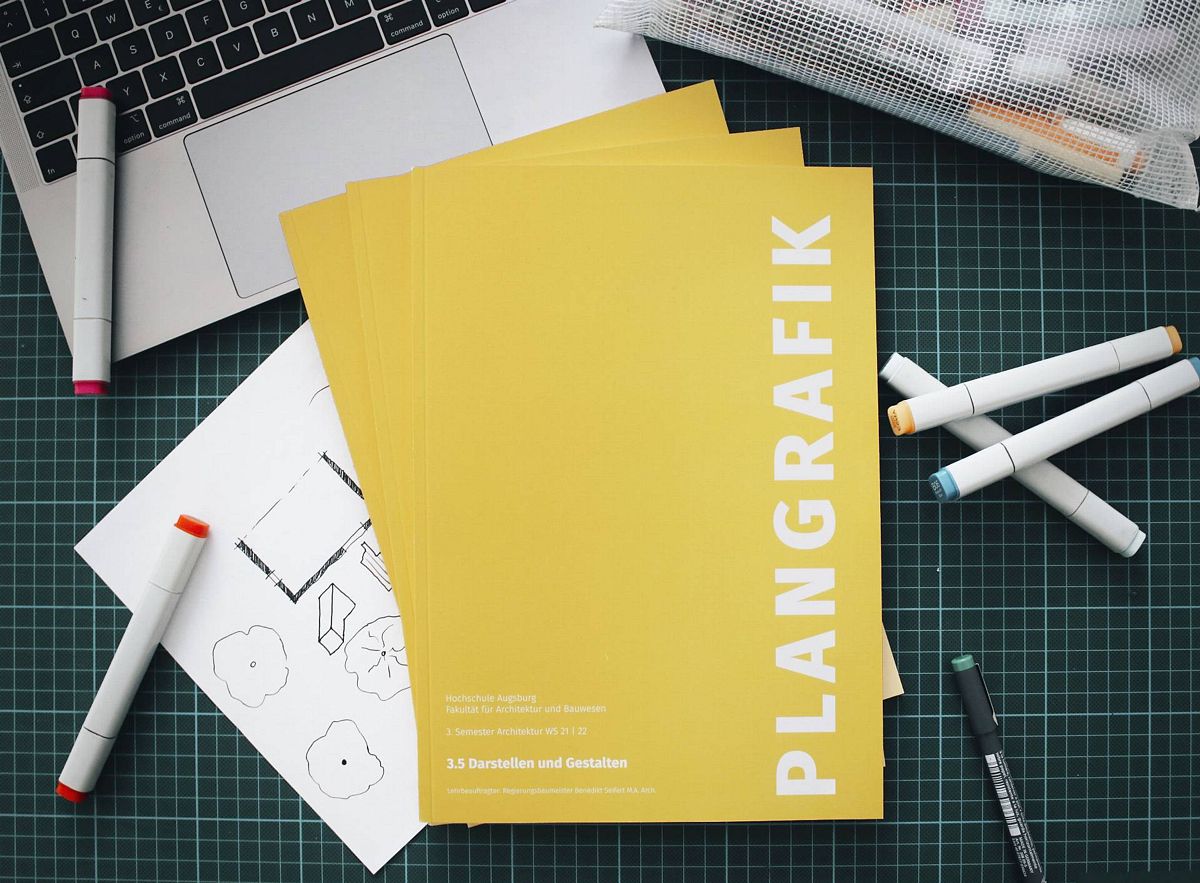 Foto des Heftes "Plangrafik" auf Schreibtisch mit Laptop und Copic-Markern