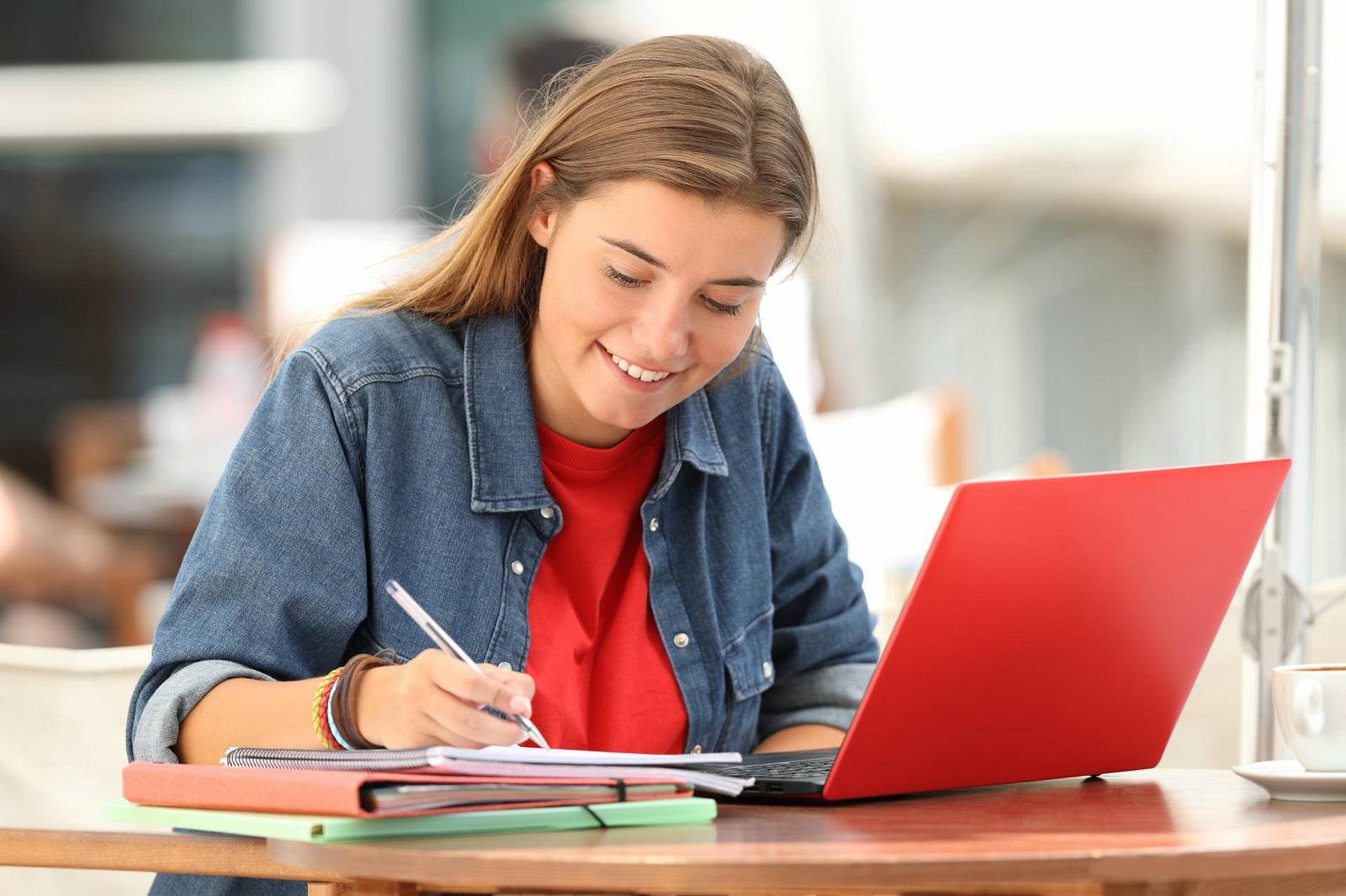 Studentin am Schreiben mit Block und Laptop