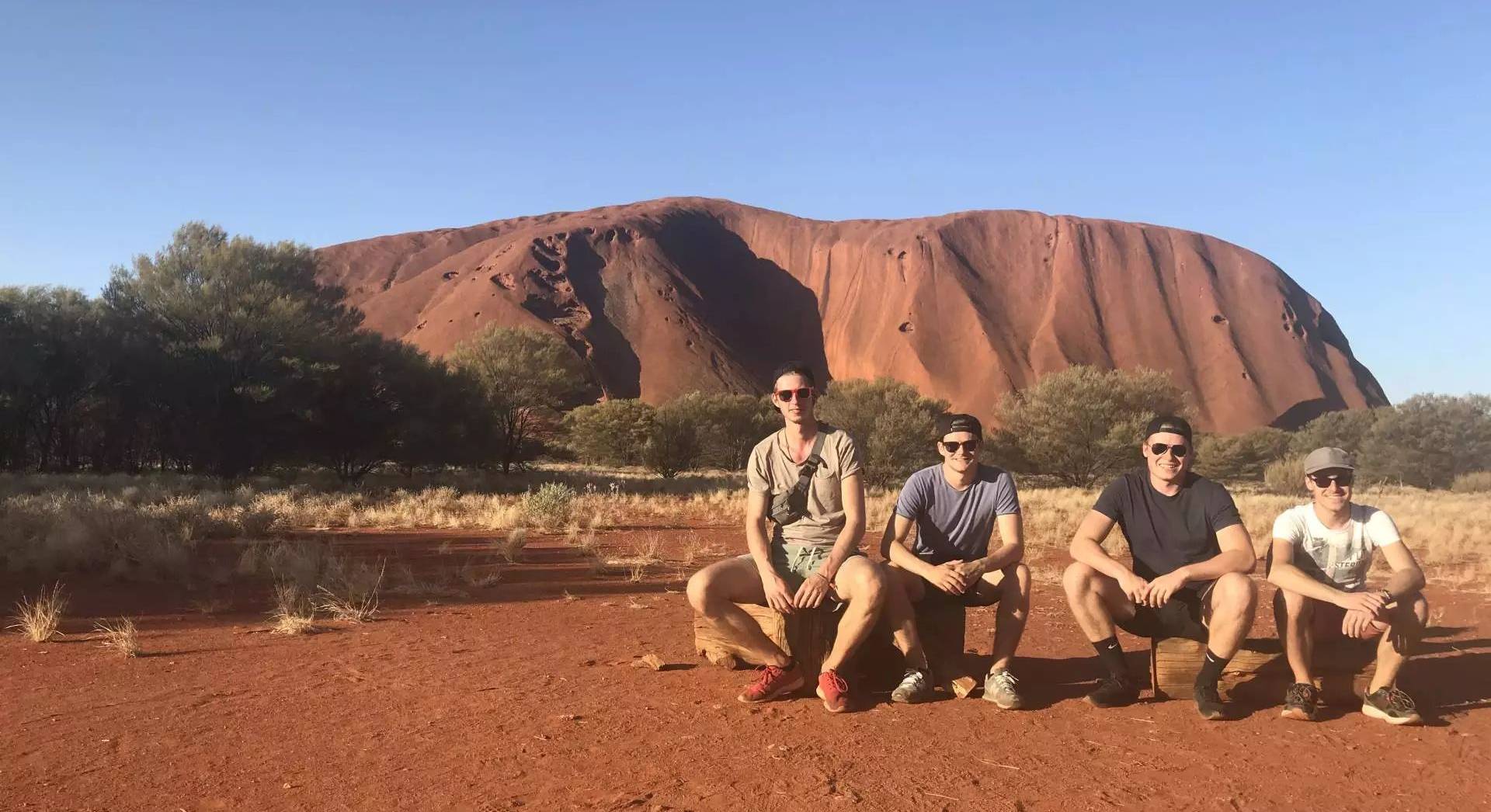 Students sitting in front of Ayers Rock in Australia